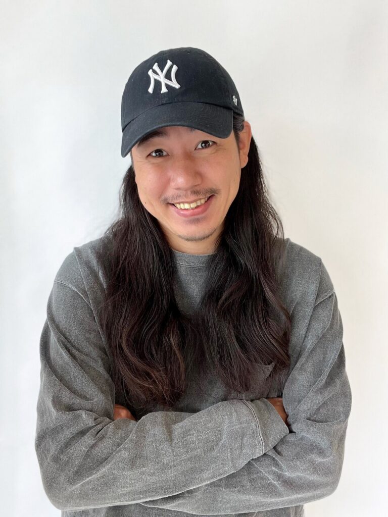 hygge+のスタッフプロフィール写真。黒いキャップとグレーの服で笑顔の男性スタッフ
